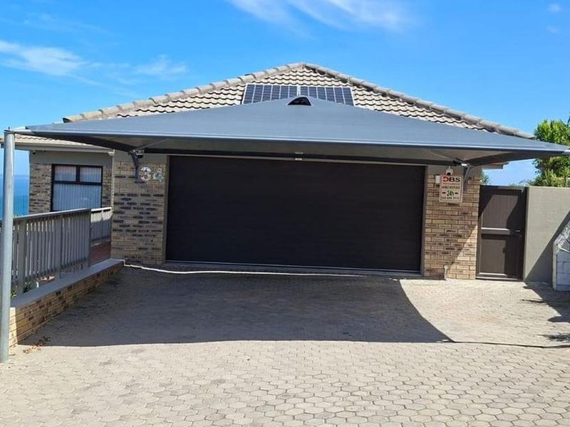 Front exterior view featuring a paved driveway, garage with a shade sail, solar panels, and stone cladding accents.