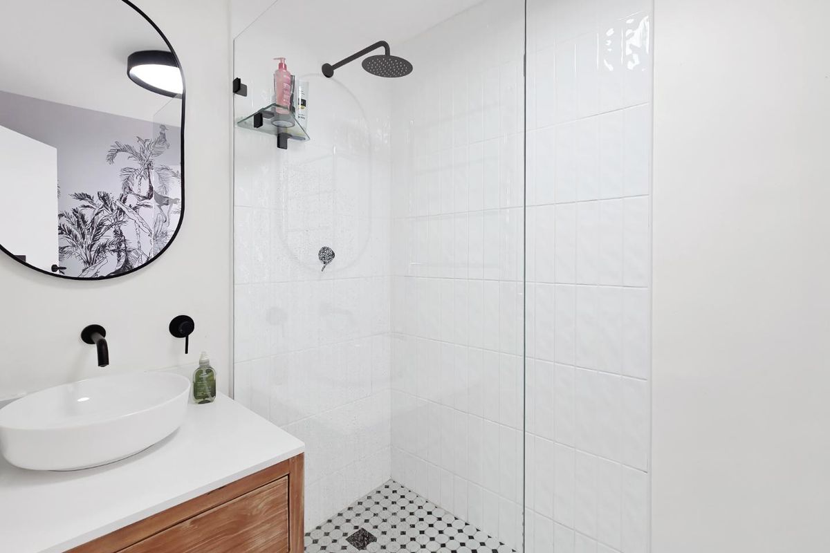 Modern bathroom featuring a wooden vanity with vessel sink, wall-mounted matte black fixtures, and a walk-in shower with glass screen and mosaic tiling.