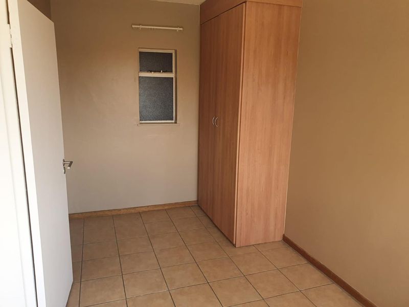 A compact, empty bedroom featuring neutral wall paint, tiled flooring, and a built-in wooden wardrobe.