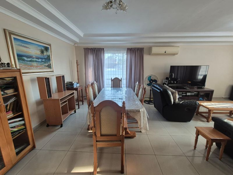 Spacious open-plan living and dining area featuring tiled flooring, decorative ceiling cornices, and a wall-mounted air conditioning unit.