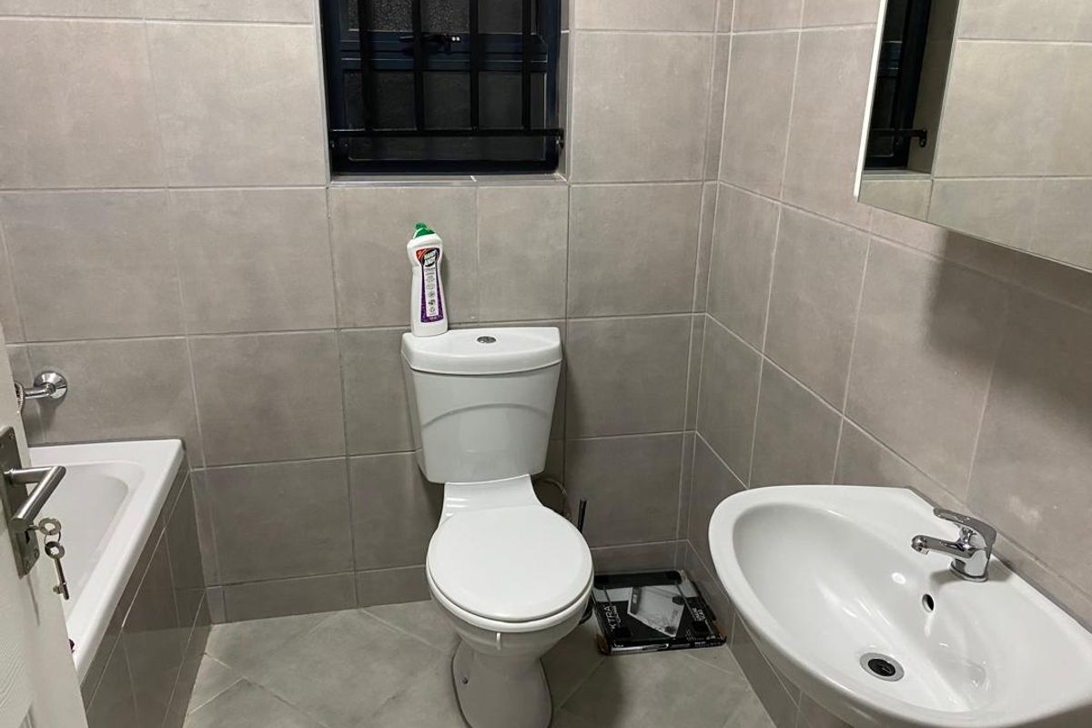 A functional bathroom featuring neutral wall tiles, a pedestal basin, a standard toilet, and a bathtub with a window.