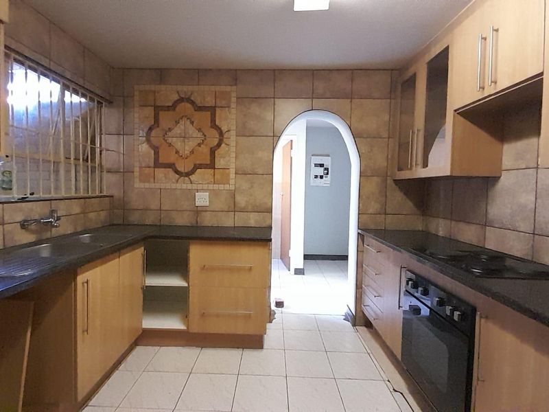 A functional kitchen featuring wood-finish cabinetry, dark countertops, built-in oven and hob, tiled backsplash, and an arched doorway leading to the rest of the home.