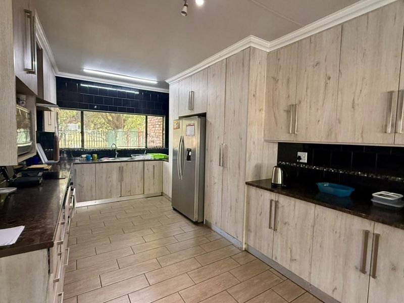 A functional kitchen featuring light wood-grain cabinetry, dark tiled backsplashes, laminate countertops, and tiled flooring with ample storage space.