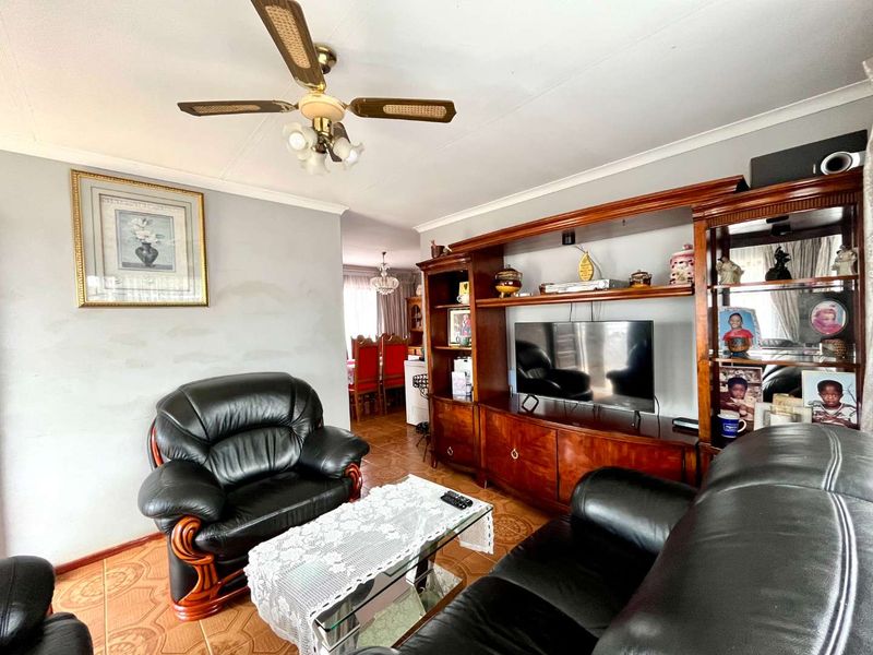 A living room featuring tiled flooring, a ceiling fan, and built-in wooden cabinetry, with an open-plan flow leading toward the dining area.