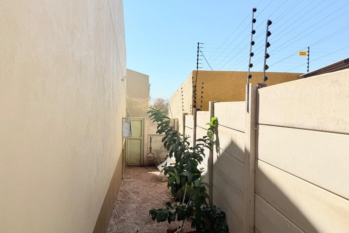 A narrow side passage featuring a precast concrete boundary wall with electric fencing and a paved walkway leading to a rear security door.