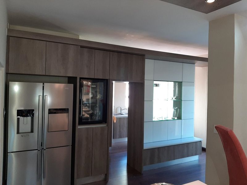 Modern kitchen featuring custom wood-tone cabinetry, integrated wine cooler, and sleek display shelving with recessed lighting.