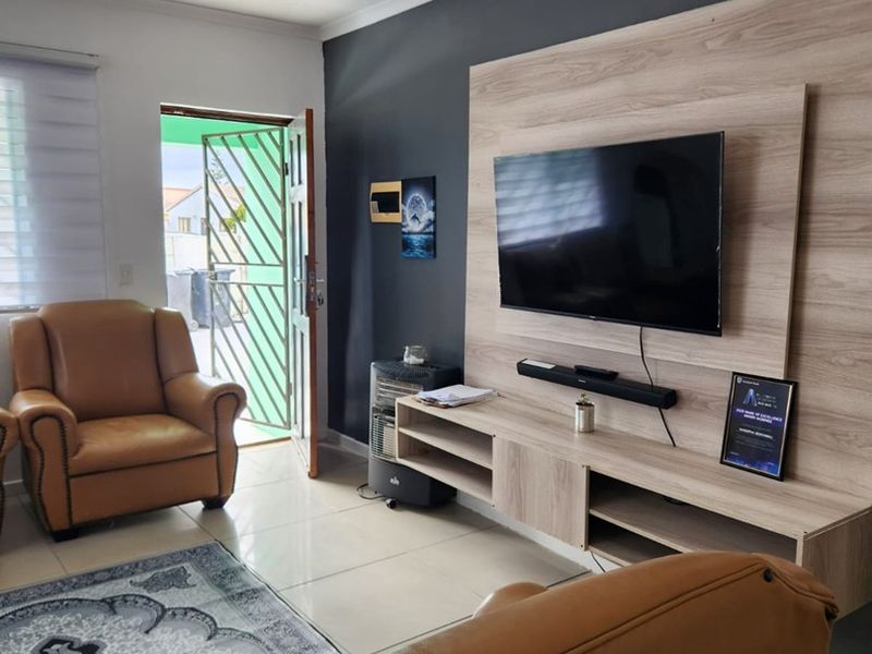 A living room featuring a modern built-in media unit, tiled flooring, and direct access to the exterior through a security gate.