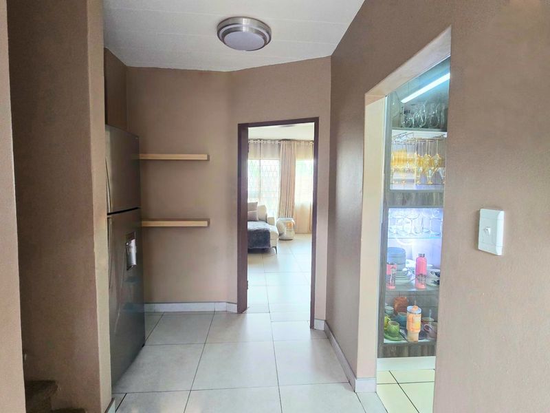 A tiled hallway featuring a built-in illuminated display cabinet and floating shelving, providing a transition between living spaces.