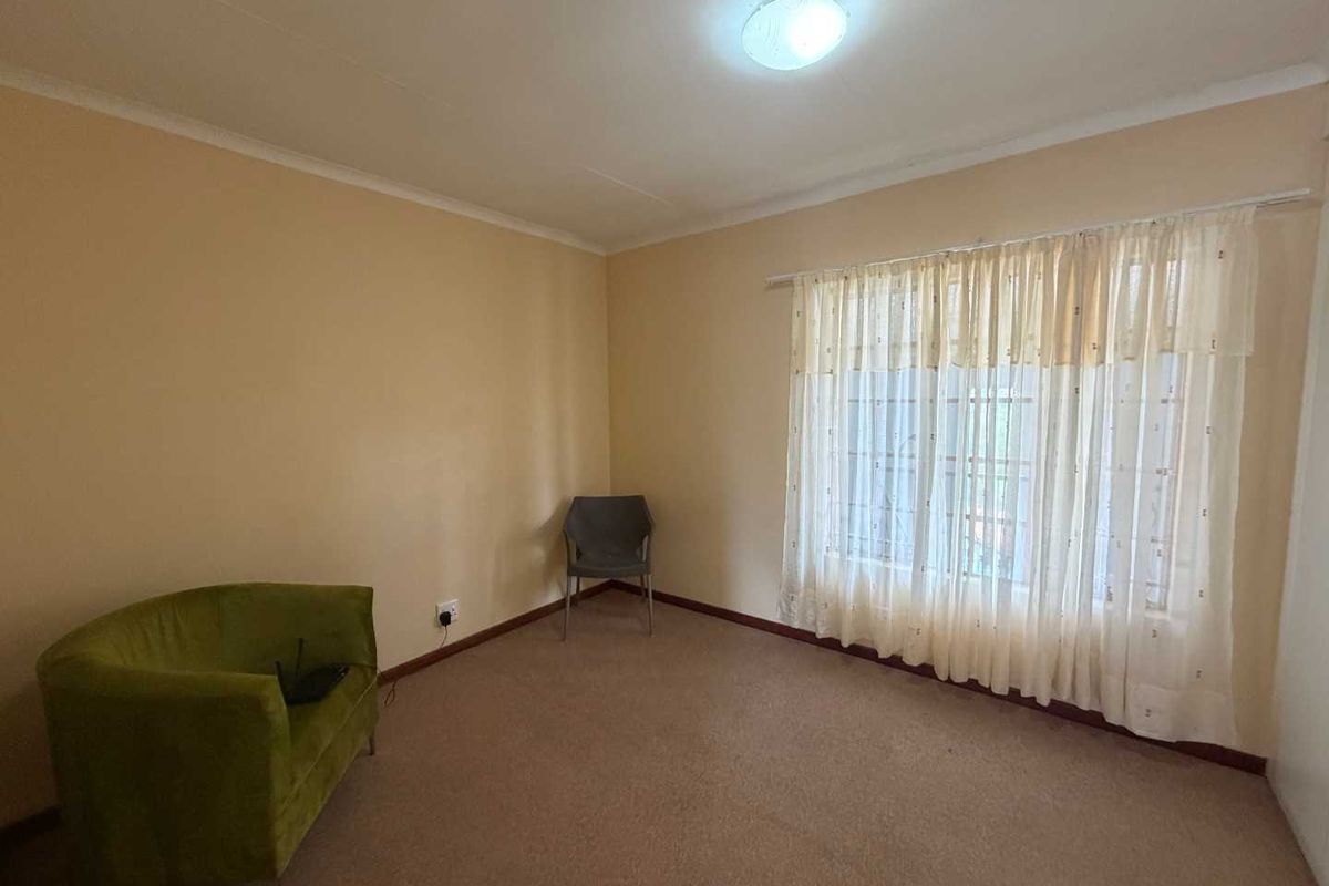 A spacious bedroom featuring neutral wall tones, carpeted flooring, and a large window with fitted curtains, providing a blank canvas for personalization.