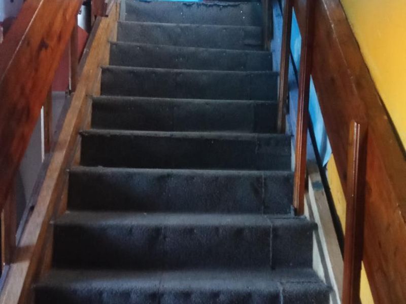 A staircase featuring timber handrails and carpeted steps, requiring cosmetic updates to the wall finishes and flooring.