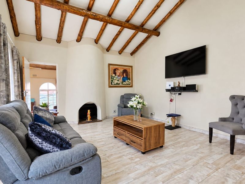 A bright living room featuring exposed timber ceiling beams, a unique built-in fireplace, and neutral tiled flooring.