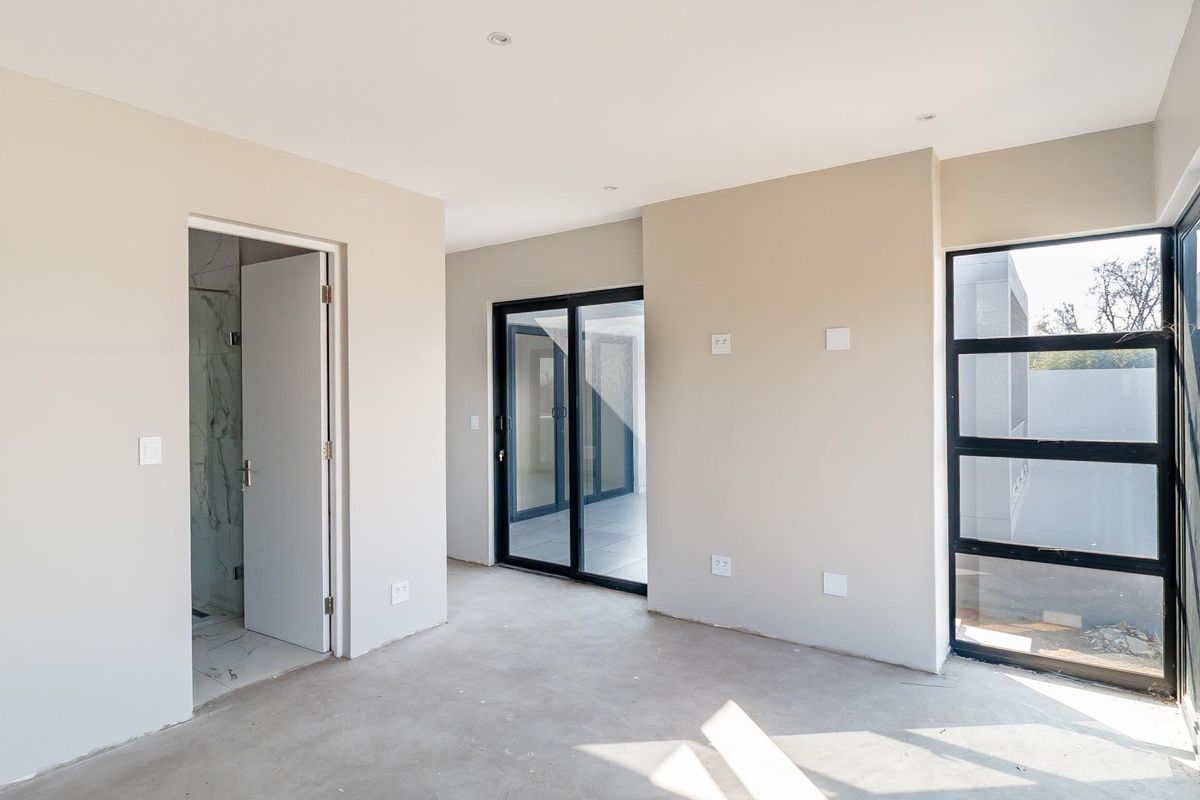 A bright, empty bedroom featuring modern aluminium sliding doors, large windows, recessed lighting, and direct access to an en-suite bathroom.
