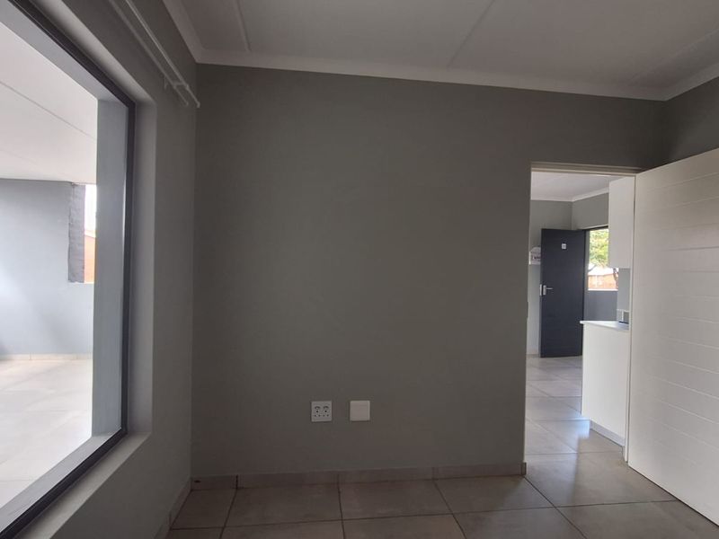 An empty living room featuring neutral grey walls, tiled flooring, and a large sliding glass door providing access to an outdoor balcony area.