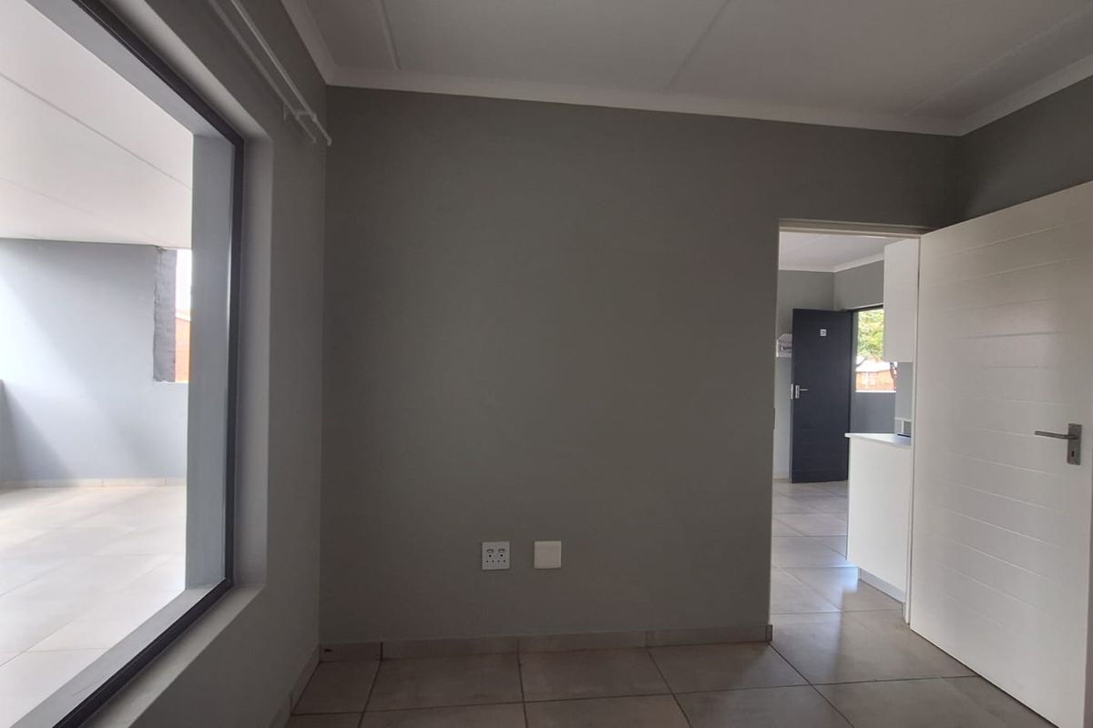An empty living room featuring neutral grey walls, tiled flooring, and a large sliding glass door providing access to an outdoor balcony area.