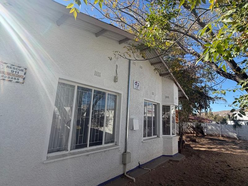 Rear exterior view of the house featuring a stucco facade, security bars on windows, and a bay window detail.