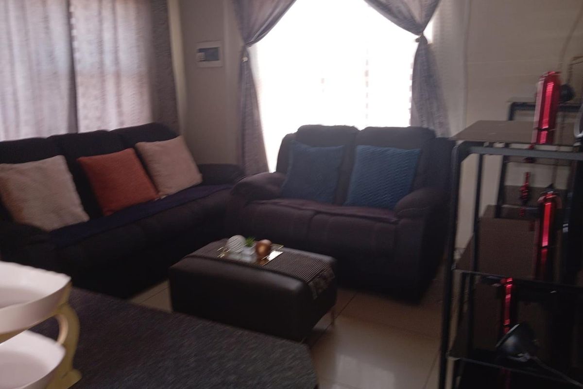 A living room area featuring tiled flooring and large windows with curtains, providing a functional space for relaxation.
