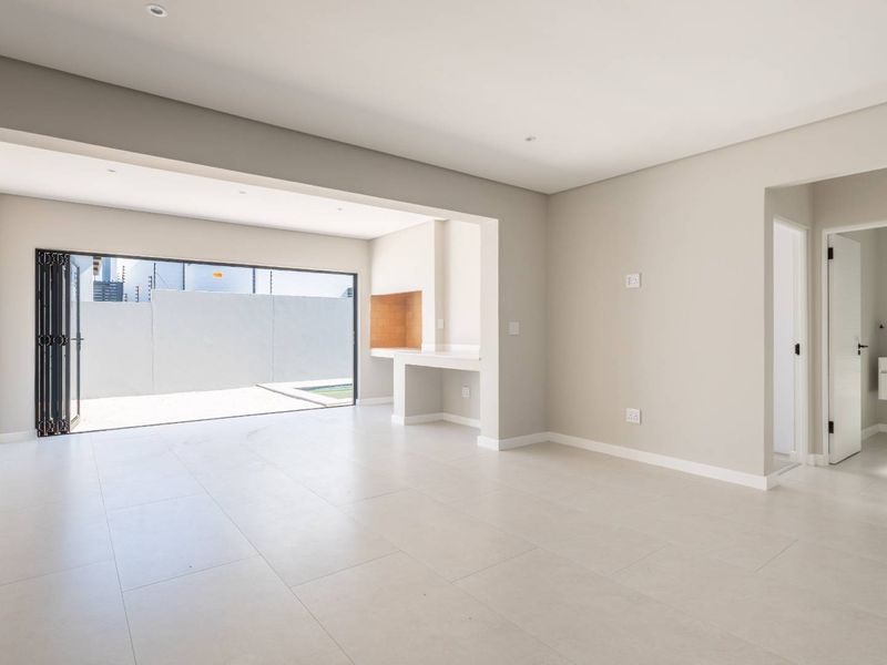 Spacious open-plan living area featuring neutral tiled flooring, recessed lighting, and a built-in braai, with seamless access to the outdoor patio area.