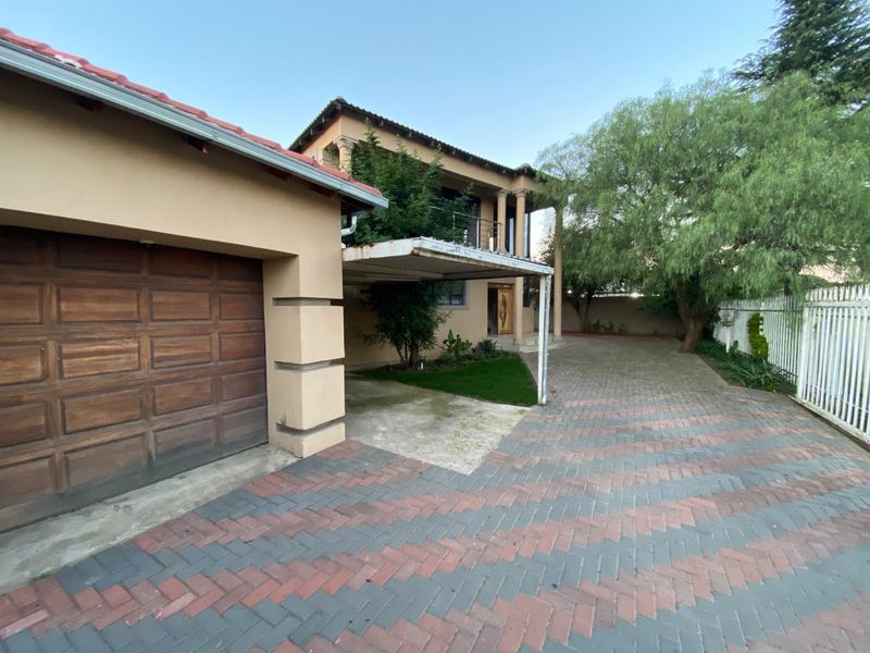 Front exterior view of a two-story house featuring a paved driveway, attached garage, carport, and balcony with columns.