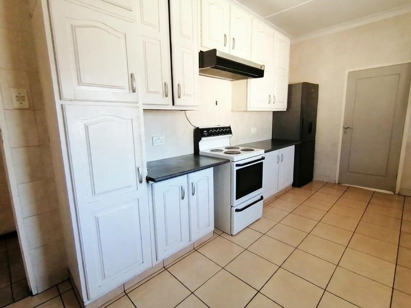 Functional kitchen featuring white cabinetry, dark laminate countertops, a freestanding stove with extractor fan, and tiled flooring.