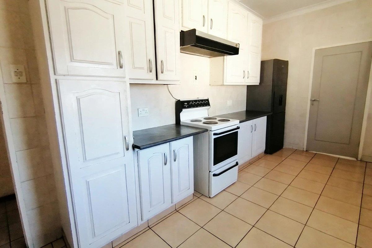 Functional kitchen featuring white cabinetry, dark laminate countertops, a freestanding stove with extractor fan, and tiled flooring.