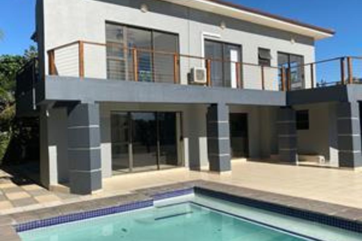 Rear view of a two-story house featuring a swimming pool, a spacious tiled patio, and an upper-level balcony with sliding glass doors.