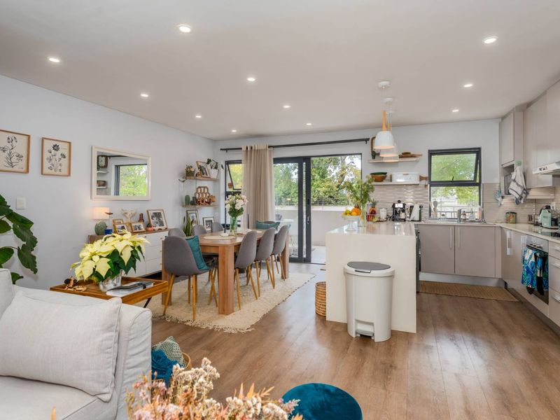 Modern open-plan living and kitchen area featuring a central island, sleek cabinetry, recessed lighting, and seamless access to an outdoor balcony.