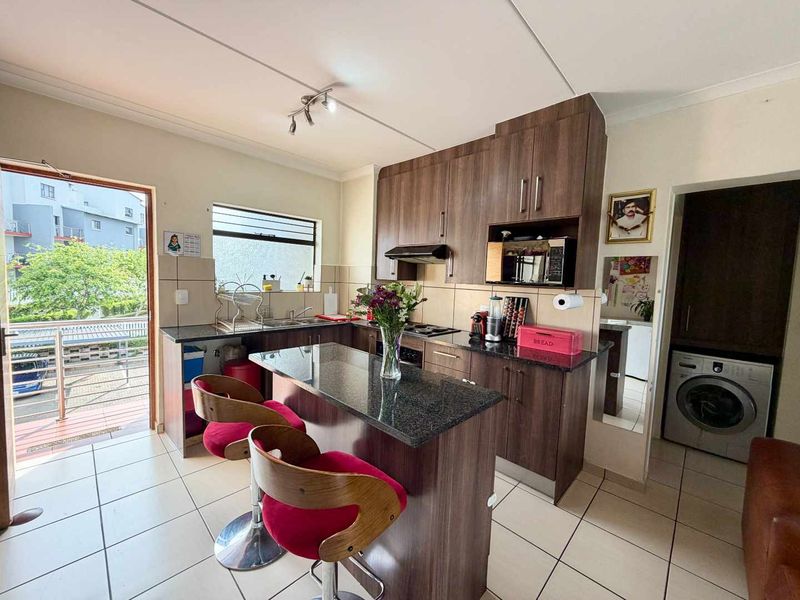 A functional kitchen featuring dark wood cabinetry, granite countertops, a breakfast bar, and integrated laundry facilities, with direct access to an outdoor balcony area.