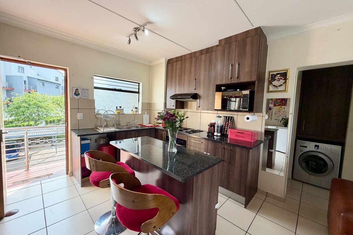 A functional kitchen featuring dark wood cabinetry, granite countertops, a breakfast bar, and integrated laundry facilities, with direct access to an outdoor balcony area.