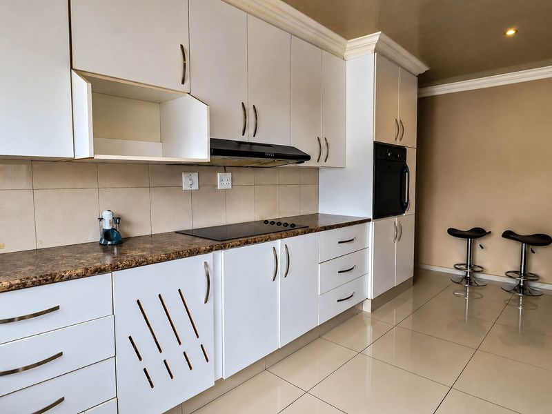 Modern kitchen featuring white cabinetry, dark laminate countertops, built-in oven, electric hob, extractor fan, and neutral ceramic floor tiles.