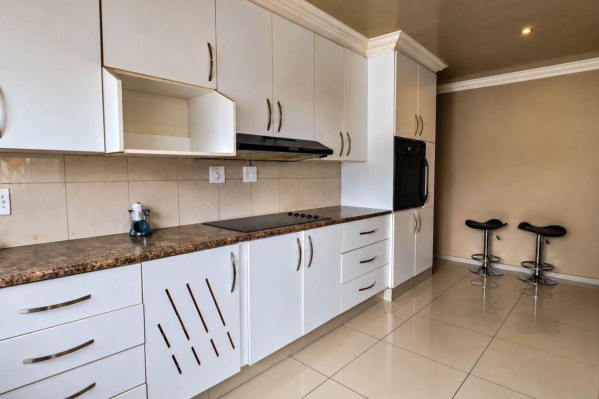 Modern kitchen featuring white cabinetry, dark laminate countertops, built-in oven, electric hob, extractor fan, and neutral ceramic floor tiles.