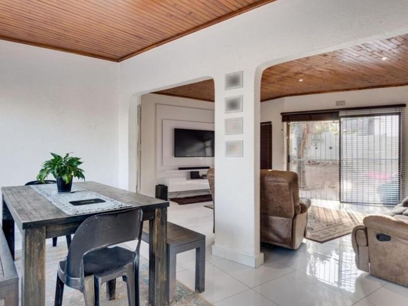 Spacious open-plan living and dining area featuring polished tiled floors, a warm timber-paneled ceiling, and sliding glass doors providing natural light and garden access.