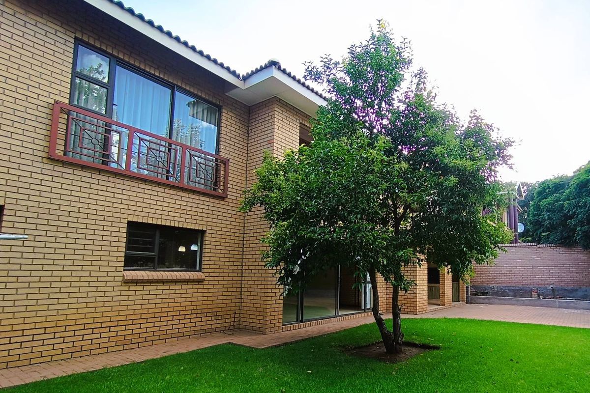 Rear view of the townhouse featuring face-brick exterior, a balcony with metal railing, sliding glass doors, and a well-maintained garden area.