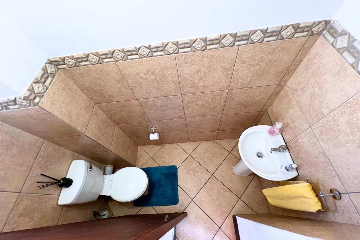 A compact guest bathroom featuring a pedestal basin, toilet, and tiled walls with a decorative border.