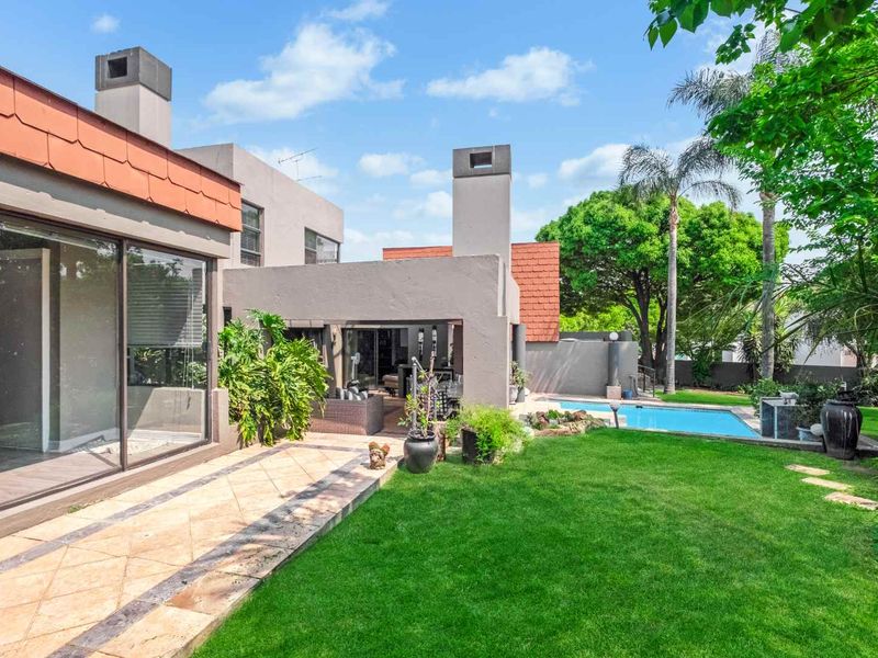 Rear view of the property featuring a landscaped garden, swimming pool, and a spacious tiled patio area with sliding door access to the home.