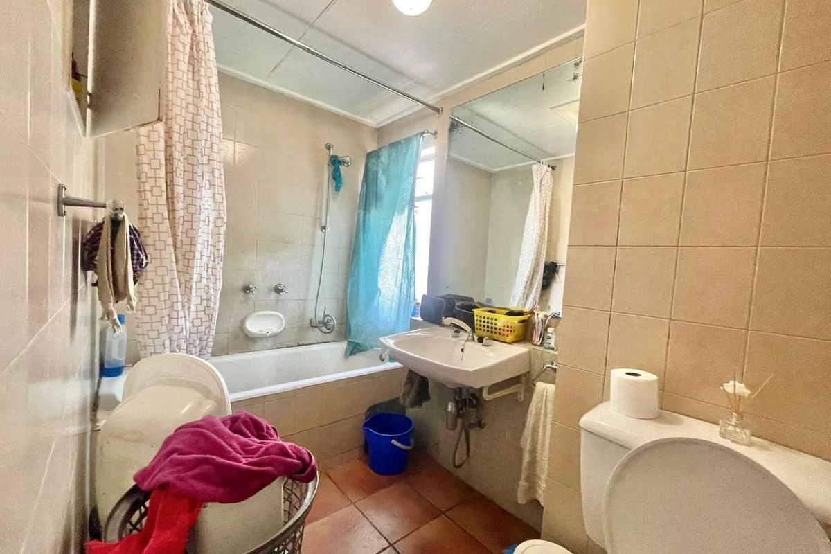 A dated bathroom featuring a bathtub with shower attachment, wall-mounted basin, and toilet, finished with neutral wall tiles and terracotta-style floor tiles.