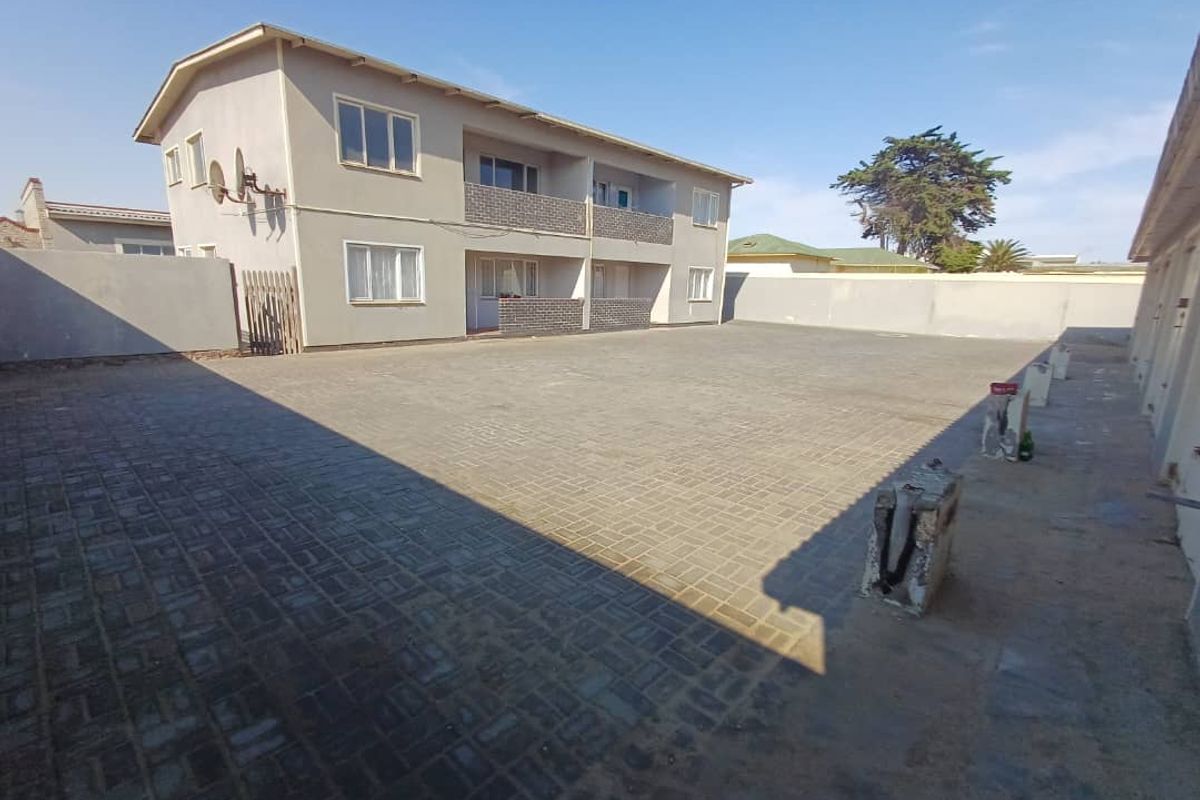 A paved rear courtyard area featuring a multi-story building facade with balconies and perimeter boundary walls.
