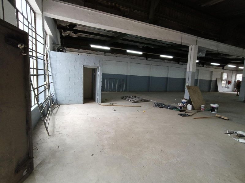 Spacious industrial utility area featuring exposed steel beams, concrete flooring, and large steel-framed windows, suitable for workshop or storage use.