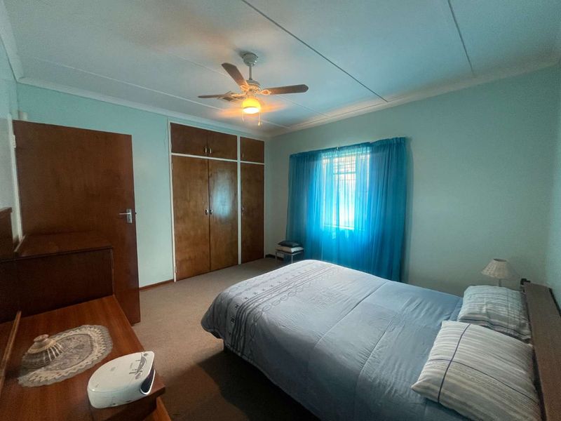 A functional bedroom featuring built-in wooden cupboards, a ceiling fan, and carpeted flooring, offering a neutral base for potential updates.