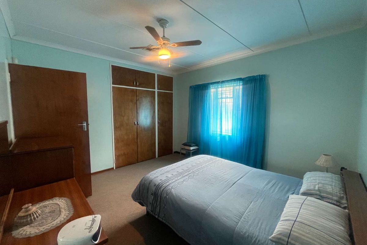 A functional bedroom featuring built-in wooden cupboards, a ceiling fan, and carpeted flooring, offering a neutral base for potential updates.