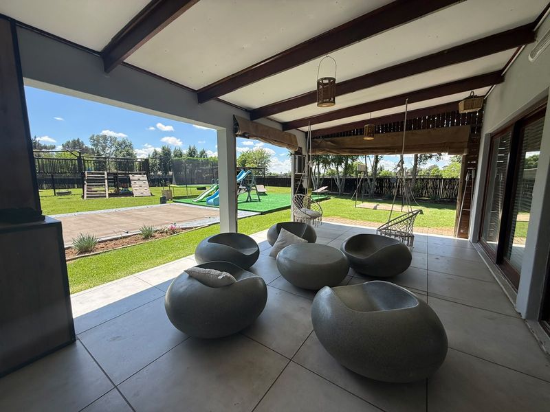A spacious covered patio featuring large format floor tiles and exposed timber beams, providing seamless access to the rear garden and play area.