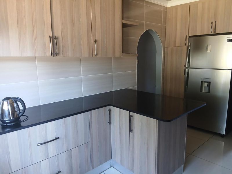 Modern kitchen featuring light wood-grain cabinetry, contrasting black granite countertops, tiled backsplash, and a distinctive arched doorway leading to adjacent space.