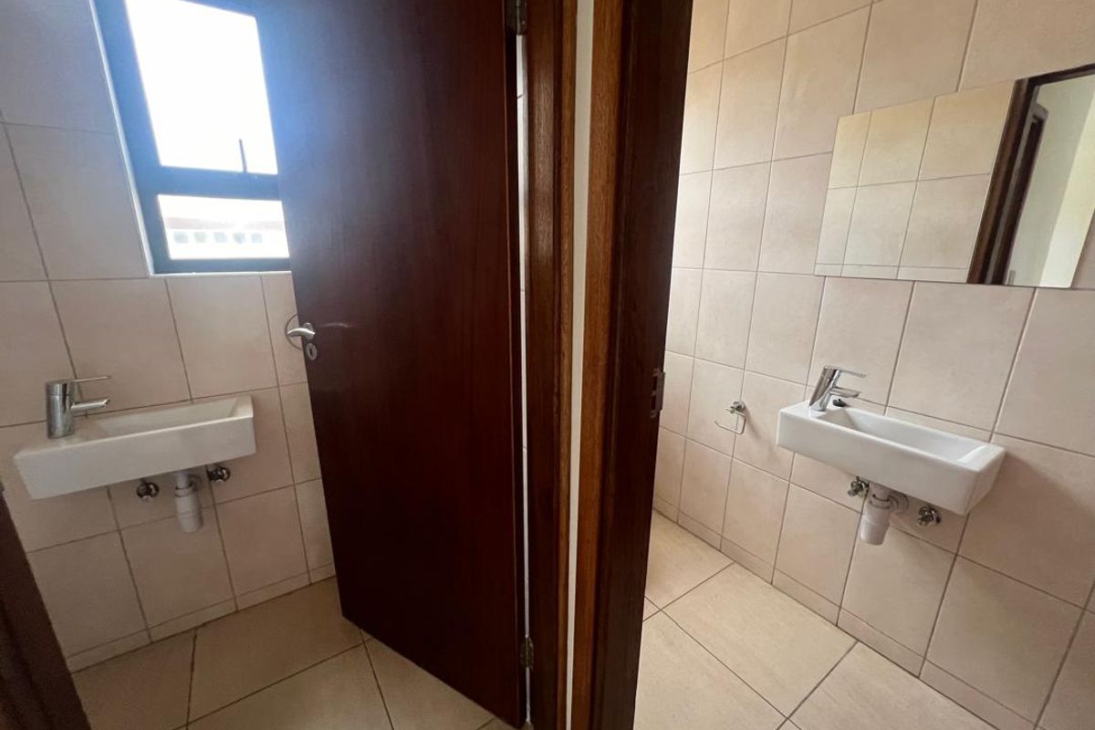 A functional industrial-style washroom area featuring two wall-mounted basins with exposed plumbing and tiled wall finishes.