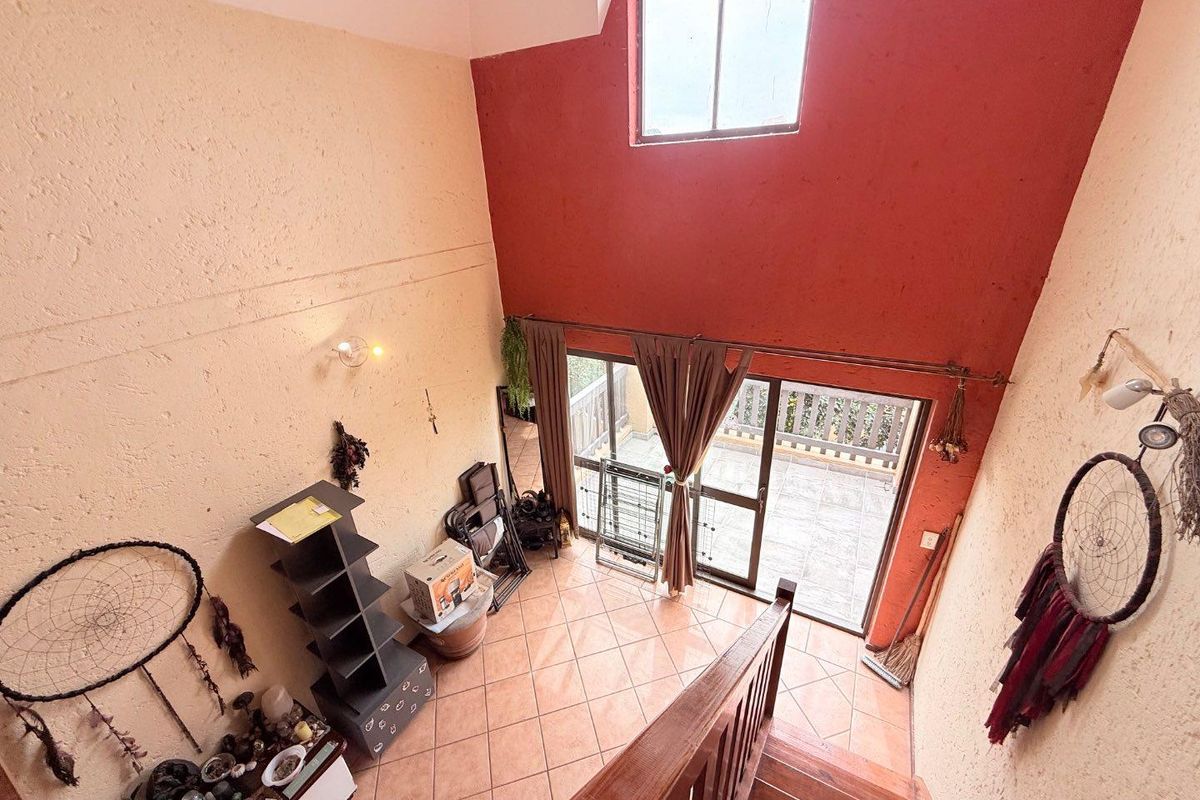 A double-volume living area featuring tiled flooring, a high ceiling with a large window, and sliding glass doors leading to an outdoor balcony.