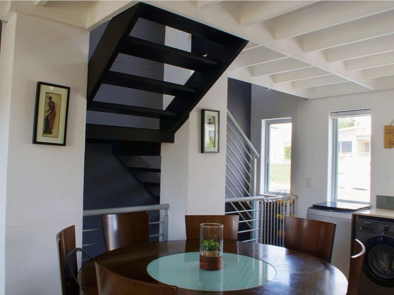 Open plan living area featuring a modern staircase, exposed ceiling beams, and integrated laundry facilities in a bright, contemporary apartment setting.