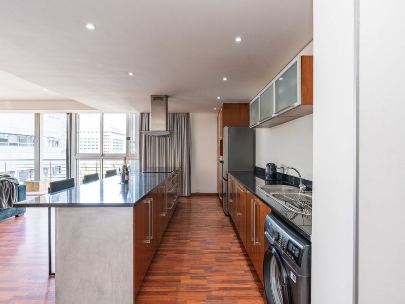 Modern open-plan kitchen featuring a large island with granite countertops, sleek wooden cabinetry, and integrated appliances, flowing into the living area.