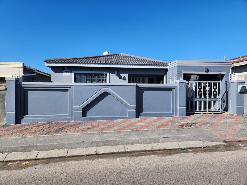 Front elevation of a residential property featuring a secure perimeter wall, gated entrance, electric fencing, and a paved driveway.