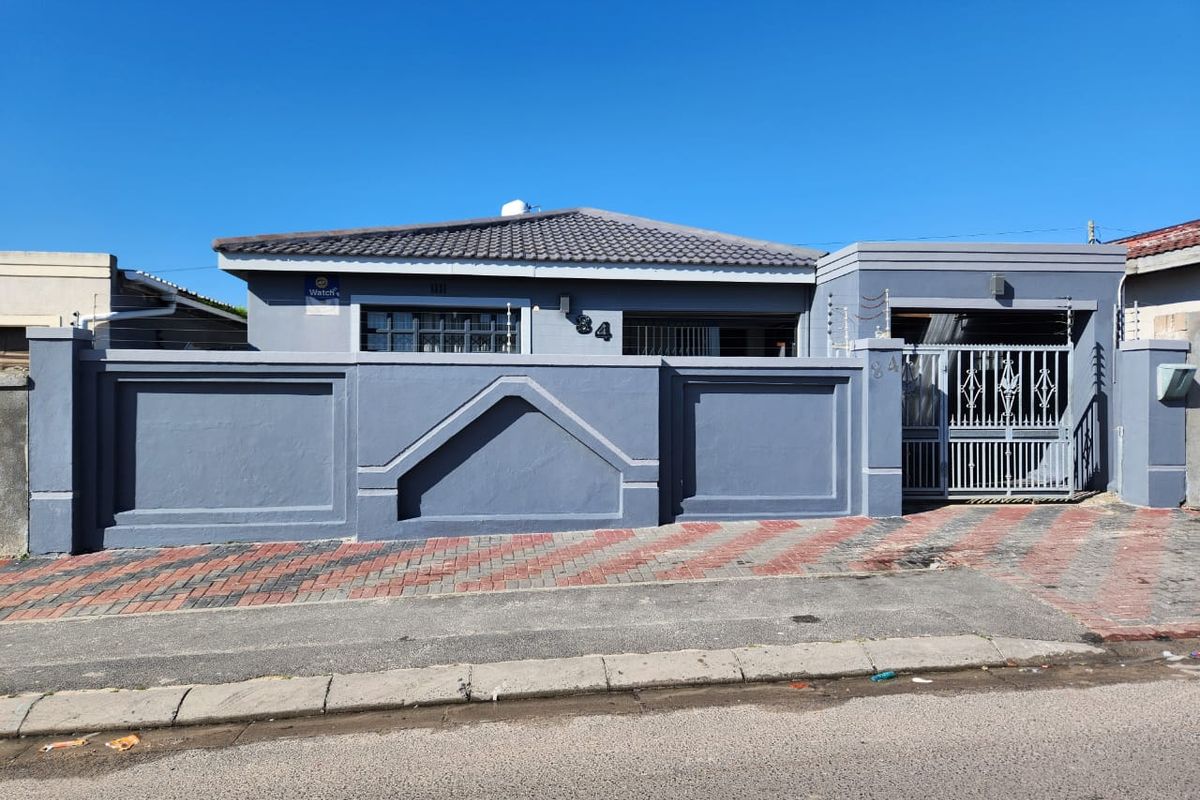 Front elevation of a residential property featuring a secure perimeter wall, gated entrance, electric fencing, and a paved driveway.