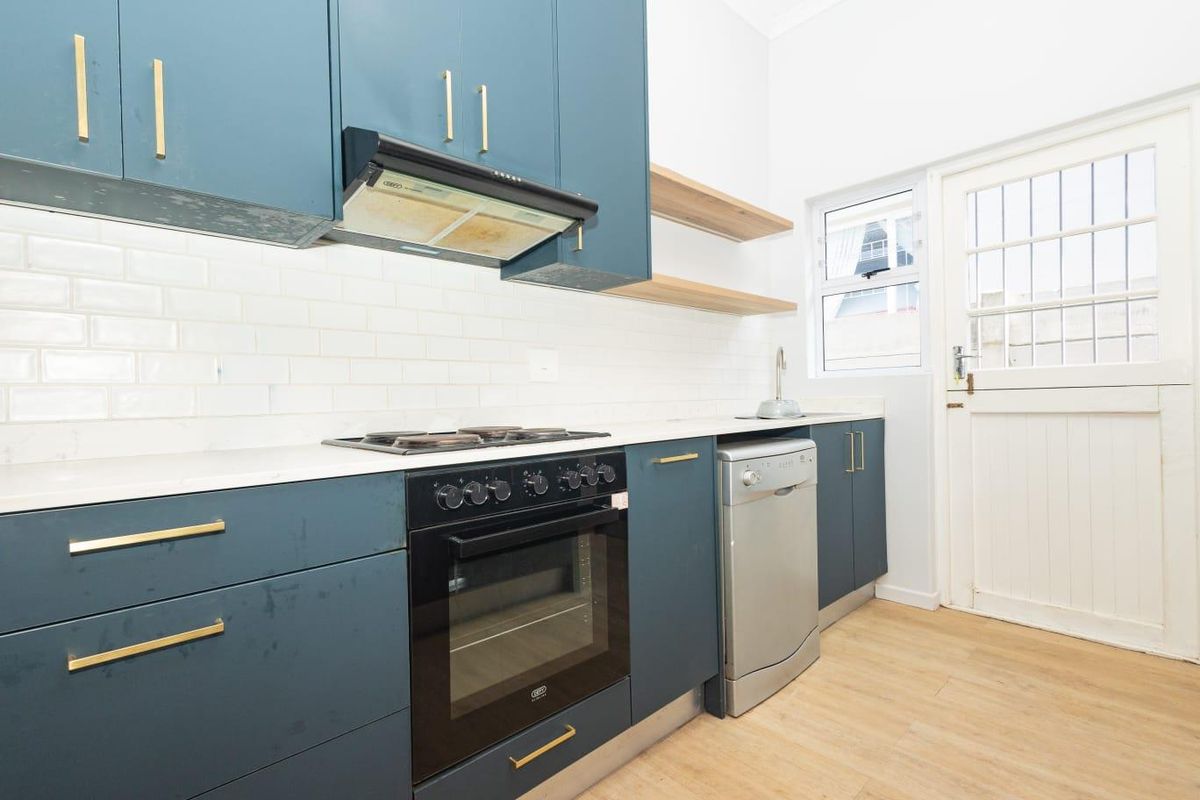 Modern kitchen featuring dark blue cabinetry, white subway tile backsplash, stone countertops, and integrated cooking appliances with direct access to the exterior.