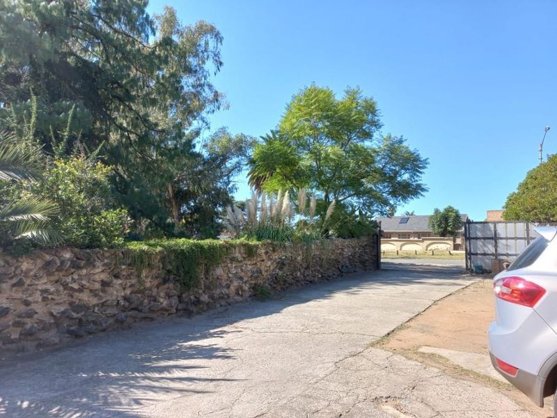 Front entrance view of the small holding featuring a stone boundary wall, concrete driveway, and gated access.