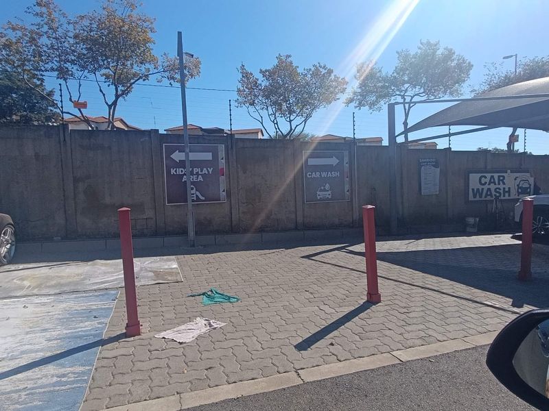 Outdoor paved area featuring a perimeter concrete wall, bollards, and signage indicating a car wash and kids' play area.